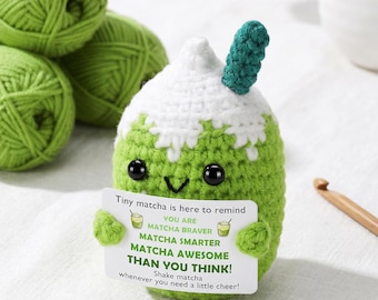 May include: A handmade green and white crochet matcha drink with black safety eyes and a small green stem. The crochet drink is holding a card that reads "Tiny matcha is here to remind... You are matcha braver, matcha smarter, matcha awesome than you think!"