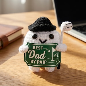 Op de afbeelding: Een wit gehaakt golf-thema karakter met een zwarte hoed, een golfclub en een groen bord met de tekst "BEST Dad BY PAR #1". Het karakter heeft zwarte knoopogen en een zwart gestikt lachje.