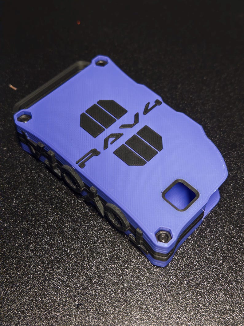 May include: A rectangular blue and black wallet with a layered, 3D-printed texture. The front features the word "RAVE" in bold black lettering, with two black rectangular accents. It includes a small square cutout and visible black screw heads.