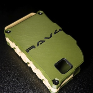 May include: A rectangular olive green phone case with a tan inner layer and black accents. The word RAVE is embossed in black on the back surface. The case features a square camera cutout and a textured finish with visible 3D printed layer lines.