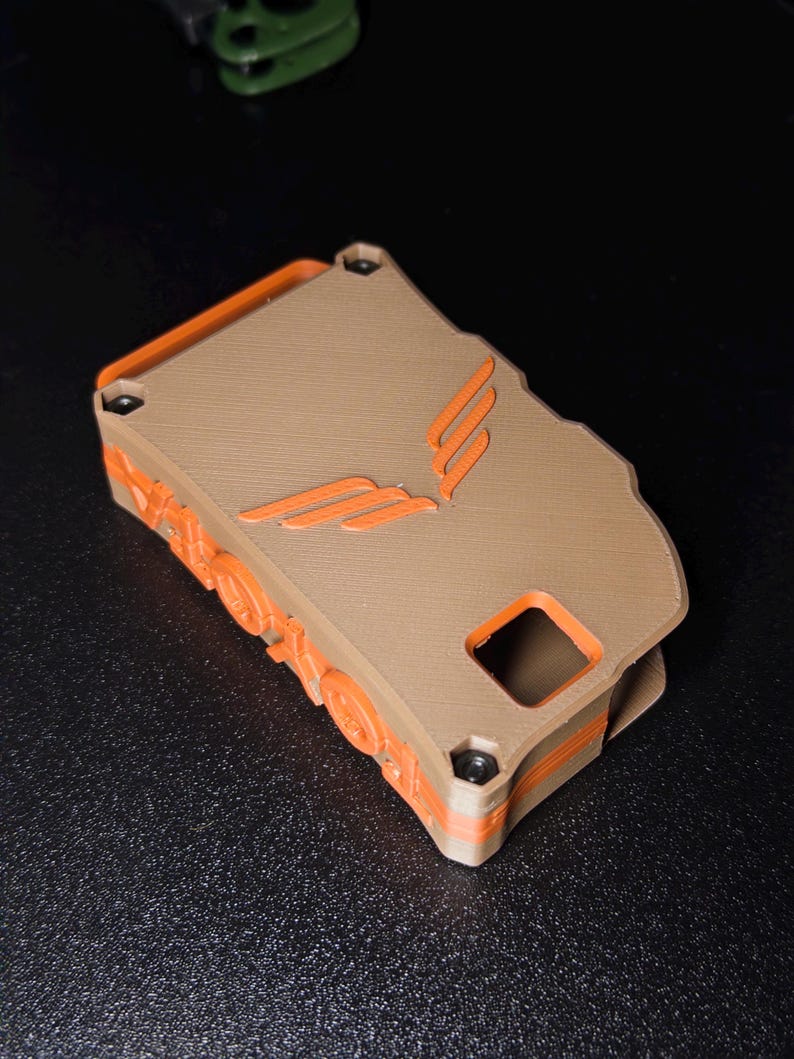 May include: A rectangular, 3D-printed case featuring a tan top panel with an embossed orange wing-like logo. The sides are orange with circular gear-like details and a square cutout. Four small black screws secure the tan top to the orange base.