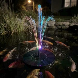 May include: A solar-powered fountain in a pond with colorful, illuminated water jets. The fountain is black and circular, with a central nozzle that sprays water upwards. Koi fish swim in the pond, and the scene is lit by a soft, warm light.