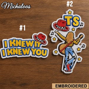Può includere: Due toppe ricamate. La toppa 1 presenta il testo I KNEW IT I KNEW YOU in giallo con contorni blu e un cappello da cowboy rosso. La toppa 2 mostra una figura bionda che suona la chitarra, indossa una camicia gialla e pantaloni con stampa mucca, con un cappello rosso, stelle gialle, note musicali e le lettere TS.