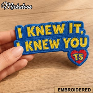 Puede incluir: Un parche bordado con fondo azul y texto amarillo que dice I KNEW IT, I KNEW YOU. El parche presenta una forma de corazón rojo en la esquina inferior derecha con las letras amarillas TS en su interior. El parche tiene un borde azul.