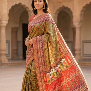 Könnte beinhalten: Ein olivgrünes und rotes Sari mit komplizierten floralen und geometrischen Mustern. Das Sari hat einen detaillierten Rand und ein lebendiges, farbenfrohes Design am unteren Teil. Der Stoff drapiert sich elegant und zeigt die satten Farben und Texturen.