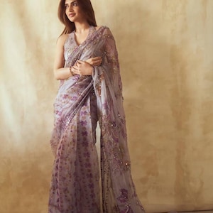May include: A light purple saree with floral patterns and sequin embellishments. The saree features a halter neckline and a flowing, sheer fabric. The design incorporates shades of purple and gold, creating an elegant and sophisticated look.