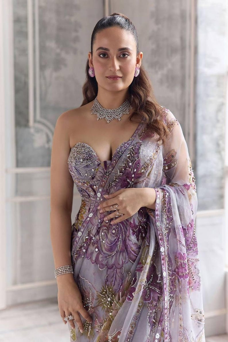 May include: A formal lavender saree with intricate floral embroidery and sequin embellishments. The saree features a strapless, embellished bodice and is paired with a matching necklace, earrings, and bracelets. The overall design is elegant and sophisticated.