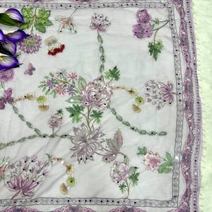 May include: A light purple scarf with intricate floral embroidery in shades of purple, pink, and green. The scarf features a delicate border with small mirrored accents. The design includes butterflies and other floral elements.