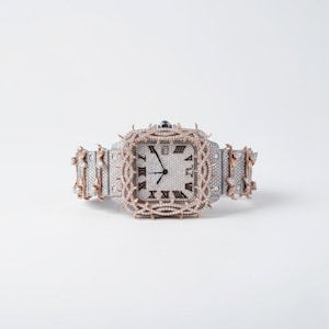 May include: A luxury wristwatch with a square face and a silver and rose gold band. The watch face features Roman numerals and is encrusted with small, sparkling stones. The bezel and band are adorned with intricate, spiky designs, adding a unique touch to the timepiece.