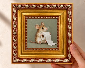 May include: A square framed painting featuring a small brown mouse sitting on a sage green surface while holding a roll of white toilet paper. The frame is ornate, featuring a metallic gold finish with silver leaf-like decorative accents.
