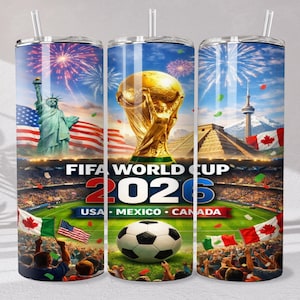 May include: A cylindrical tumbler with a straw featuring a FIFA World Cup 2026 graphic. The design includes the Statue of Liberty, the World Cup trophy, a soccer ball, stadium crowds, and flags of the USA, Mexico, and Canada under fireworks.