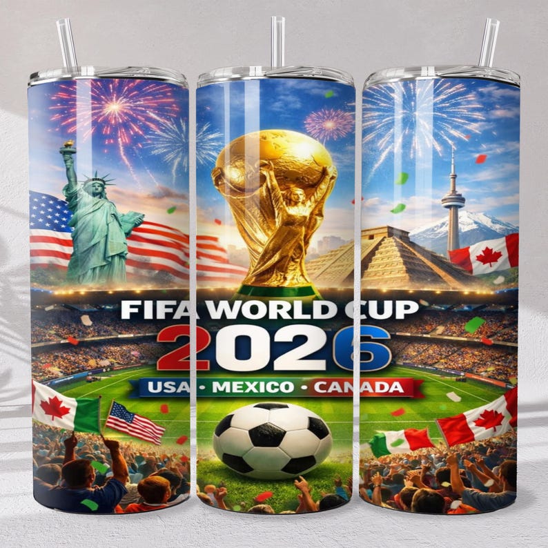 May include: A cylindrical tumbler with a straw featuring a FIFA World Cup 2026 graphic. The design includes the Statue of Liberty, the World Cup trophy, a soccer ball, stadium crowds, and flags of the USA, Mexico, and Canada under fireworks.