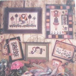 May include: A collection of cross-stitch patterns featuring a garden theme. The patterns include a girl with a watering can, a birdhouse, and a flower. The text "89501 GARDEN TREASURES FIBER MOSAICS™" is printed on the bottom of the image.