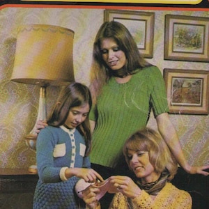 May include: A vintage book cover for a knitting and crocheting guide called "Woolcraft" with a new crochet section. The cover features three women knitting and crocheting, with a lamp and framed pictures in the background.