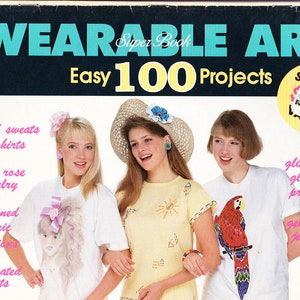 May include: A book cover with the title "Wearable Art Easy 100 Projects" in blue and yellow text. Three girls are shown wearing decorated shirts. The book cover features a price tag with the price of £4.95.