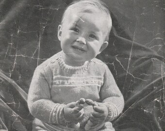 May include: Black and white photograph of a baby wearing a knitted sweater and trousers. The baby is sitting on a textured surface and holding a toy. The photo is from a vintage knitting pattern leaflet titled "Paragon Baby's Suit".