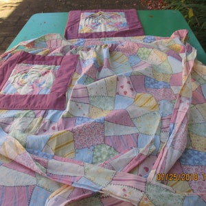 May include: A patchwork quilt apron with a pink and white floral design. The apron has a large pocket on the front and is tied at the waist.