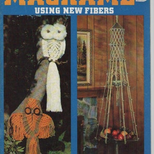 May include: A vintage book cover with the title "Macrame'" in orange letters on a blue background. The image features macrame owl decorations and a hanging plant holder filled with fruit. The text "Using New Fibers" is also present.