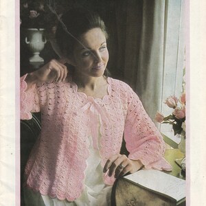 May include: A pink crocheted bed jacket with a scalloped edge and a bow tie. The jacket is worn by a woman sitting by a window. The text "Good night & good morning" and "Bed jackets in Patons yarns" is visible in the image. The text "Book 861 Patons" is also visible in the image.