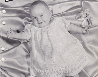 May include: Black and white photograph of a baby wearing a white knitted dress. The baby is holding a bunch of flowers and is lying on a satin fabric. The image is from a knitting book titled "Villawool Knitting Book No. 51".