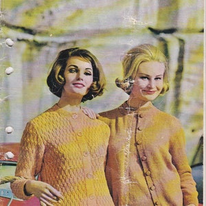 Peut inclure: Deux femmes portant des cardigans en tricot jaune et orange. Le cardigan à gauche a un motif en tricot torsadé. Le cardigan à droite a un motif en tricot lisse. Les femmes sont debout devant une voiture et un mur de briques. Le texte "BOOK 107" est en haut de l'image. Le texte "LADY'S DESIGNS IN 5, 8 AND 12 PLY EQUIVALENTS BY Lillawool" est sur le côté droit de l'image. Le texte "2'9" est dans un cercle en bas à droite de l'image.