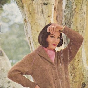 May include: A brown cardigan with a collar and pockets. The cardigan is worn by a woman with dark hair and a pink scarf. The image is from a knitting pattern book titled "Book 121" by Villawool. The price is 2/9 or 28c.