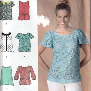 May include: Simplicity sewing pattern with multiple blouse designs. A woman models a light blue lace top. The pattern includes various blouse styles with short sleeves and other design variations. The pattern sizes are U.S. 4, 6, 8, 10, and 12, with a French size range of 32-40.