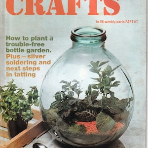May include: A magazine cover for Golden Hands Encyclopedia of Crafts, featuring a clear glass bottle terrarium with green plants and red gravel. The cover text reads "How to plant a trouble-free bottle garden. Plus - silver soldering and next steps in tatting."
