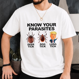 May include: A white short-sleeved t-shirt featuring the black text "KNOW YOUR PARASITES" above three illustrations: a brown deer tick, a brown dog tick, and a cartoon figure labeled "LUNA TICK" with the text "DEER TICK" and "DOG TICK" below.