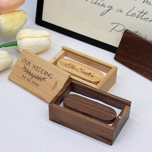 Puede incluir: Unidades flash USB de madera en cajas decorativas. Una caja está grabada con "OUR WEDDING" y la fecha "06.22.2026". Otra caja está grabada con "The Smith's". Las cajas son de madera clara y oscura.