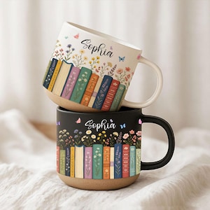 Puede incluir: Dos tazas de cerámica, una blanca y otra negra, apiladas. Ambas tazas presentan un diseño floral y de libros con el nombre "Sophia". La taza blanca tiene un asa blanca, y la taza negra tiene un asa negra. Las tazas tienen una base de color natural.