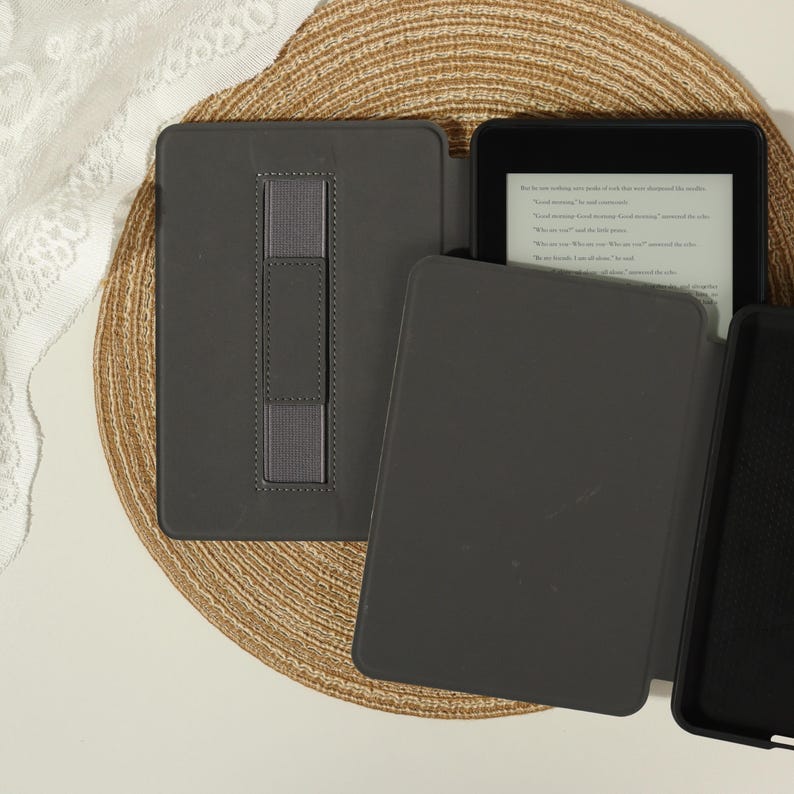 Puede incluir: Una funda para lector electr&oacute;nico de color gris oscuro con una correa el&aacute;stica vertical en la cubierta trasera. El conjunto incluye una cubierta protectora gris oscuro a juego con acabado liso y marco interior negro, junto a un lector con texto.