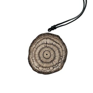Puede incluir: Colgante redondo de madera con un cordón negro. El colgante presenta círculos concéntricos y líneas radiales, que se asemejan a una sección transversal de un tronco de árbol. El colgante es de color marrón natural.