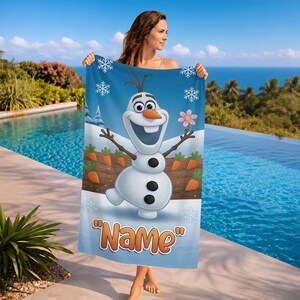 May include: A blue beach towel featuring Olaf the snowman from Frozen, with a carrot garden and snowflakes. The towel has the word "Name" in orange text at the bottom. The background shows a pool and ocean.