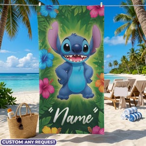 May include: A beach towel featuring a cartoon character with large ears, surrounded by colorful flowers and tropical foliage. The towel has the word "Name" in a script font. The background shows a beach scene with palm trees and the ocean.