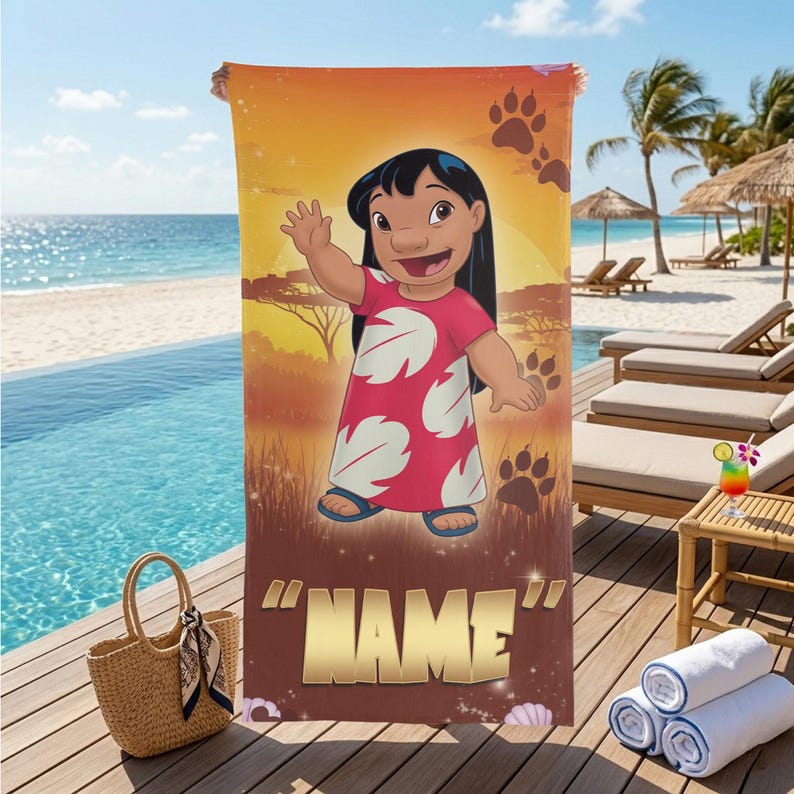 May include: A beach towel featuring a cartoon character in a red dress with white leaf patterns, set against a sunset scene with paw prints. The towel has the word "NAME" in gold letters at the bottom. A straw bag and rolled towels are in the foreground.