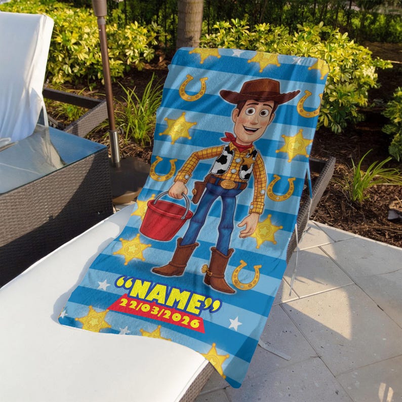 May include: A blue and white striped beach towel featuring a cartoon image of Woody from Toy Story. The towel has yellow stars and horseshoes, with the text "NAME" and a date. The towel is draped over a lounge chair.