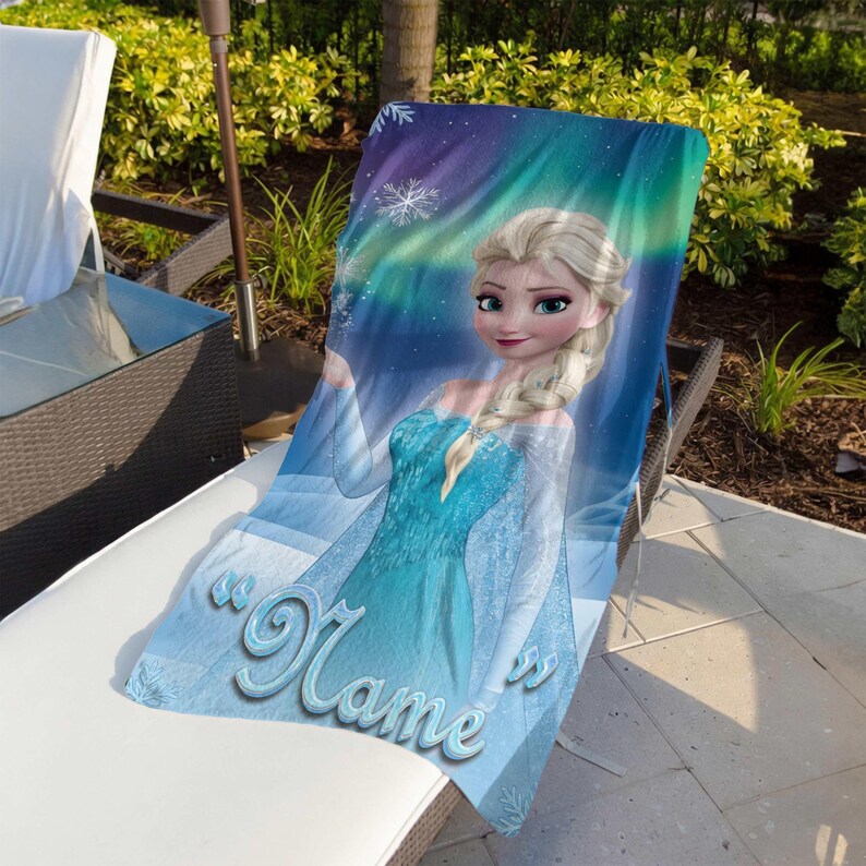 May include: A blue beach towel featuring a cartoon image of a blonde woman in a blue dress. The towel has the word "Name" in a cursive font. The background has a blue and purple aurora borealis design with snowflakes.