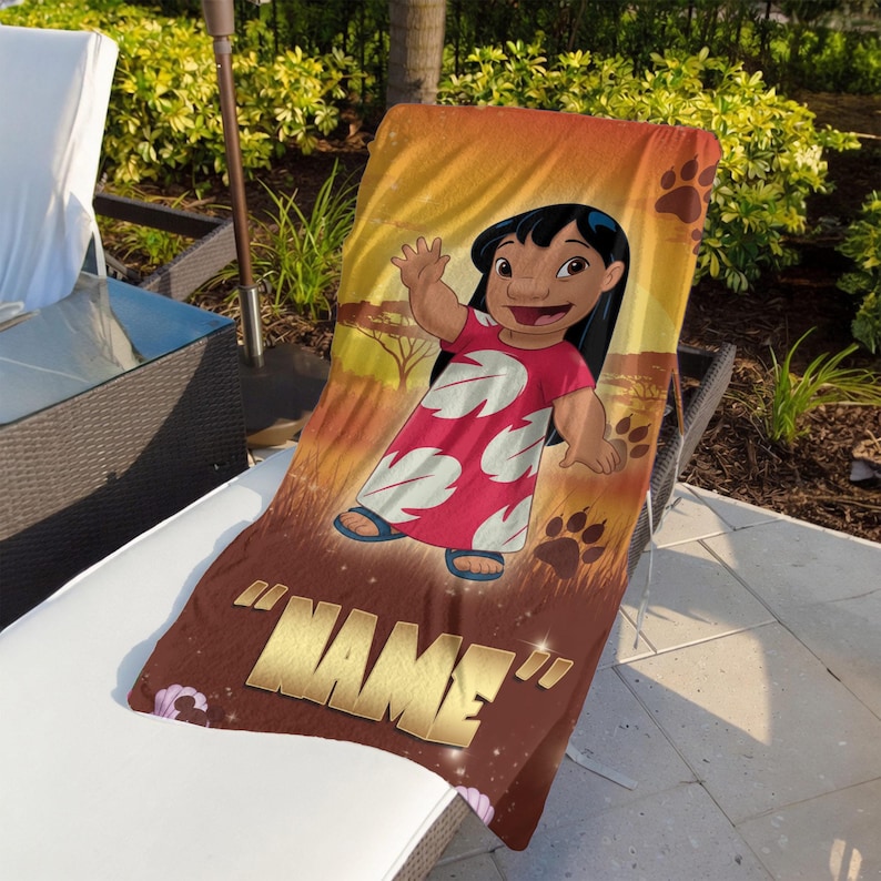 May include: A beach towel featuring a cartoon character in a red dress with white floral designs, waving. The towel has a brown background with paw prints and the word "NAME" in gold lettering. The towel is draped over a white lounge chair.