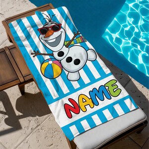 K&ouml;nnte beinhalten: Ein Strandtuch mit blau-wei&szlig;en Streifen, das einen Cartoon-Schneemann mit Sonnenbrille und einem Strandball zeigt. Das Wort "NAME" ist in bunten Buchstaben am unteren Rand aufgedruckt. Das Handtuch liegt auf einer Holzliege.