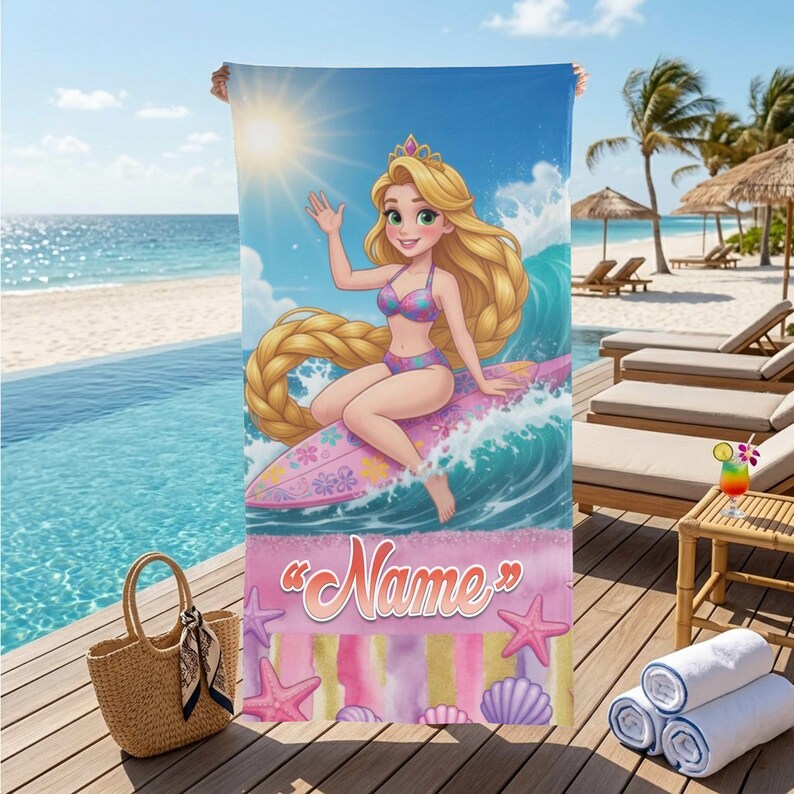 Op de afbeelding: Strandlaken met een cartoonprinses die op een golf surft. De handdoek heeft een blauwe hemelachtergrond met een zon en een roze en paarse rand met het woord "Name". Decoratieve zeeschelpen en zeesterren zijn ook afgebeeld.