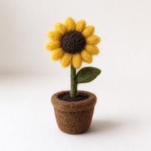 May include: A handcrafted felt sunflower in a brown felt pot. The sunflower has yellow petals and a dark brown center. The green stem supports a single green leaf. The pot is filled with brown felt to simulate soil.