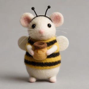 Könnte beinhalten: Eine handgefertigte Filzmaus, die als Biene verkleidet ist und einen kleinen Honigtopf hält. Die Maus hat einen weißen Körper, rosa Ohren und Nase sowie schwarze Augen. Sie trägt eine gelb-schwarz gestreifte Weste, kleine weiße Flügel und schwarze Antennen.