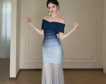 May include: An off-the-shoulder, ombre-effect gown. The dress transitions from a deep navy blue at the top to a light blue and then a sheer, flowing skirt. The dress is form-fitting through the bodice and waist, with a floor-length skirt.