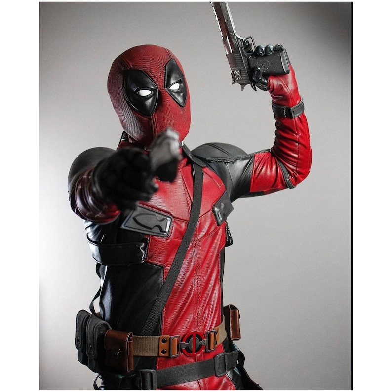 May include: A red and black Deadpool costume with a mask, gloves, and utility belt. The character is holding a gun in one hand and pointing with the other. The costume has a leather-like appearance.