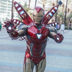 May include: A full-body Iron Man costume in red and gold, with a helmet and glowing hand repulsors. The costume has multiple wing-like structures on the back and a chest arc reactor. A small camera is attached to the back.