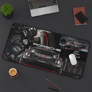May include: Black rectangular desk mat featuring a Porsche race car design. The mat includes the Porsche logo and text, along with images of car components and the text "Need Money for Porsche". A white mouse is on the mat.