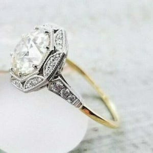 May include: A ring featuring a large, oval-cut center stone surrounded by a halo of smaller, round-cut stones. The setting is crafted from silver-toned metal, while the band is made of a thin, polished gold-toned metal, creating a two-tone design.