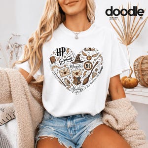 Könnte beinhalten: Weißes T-Shirt mit herzförmigem Design mit Harry-Potter-Illustrationen. Das Design umfasst eine Brille, einen Blitz, einen Hut und die Worte "Always" und "Muggles". Das T-Shirt hat kurze Ärmel.