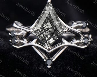 May include: A silver engagement ring set with a unique design. The ring features a large, clear, triangular-cut stone with black inclusions, and is accented with small black stones. The band has an intricate, branch-like design.